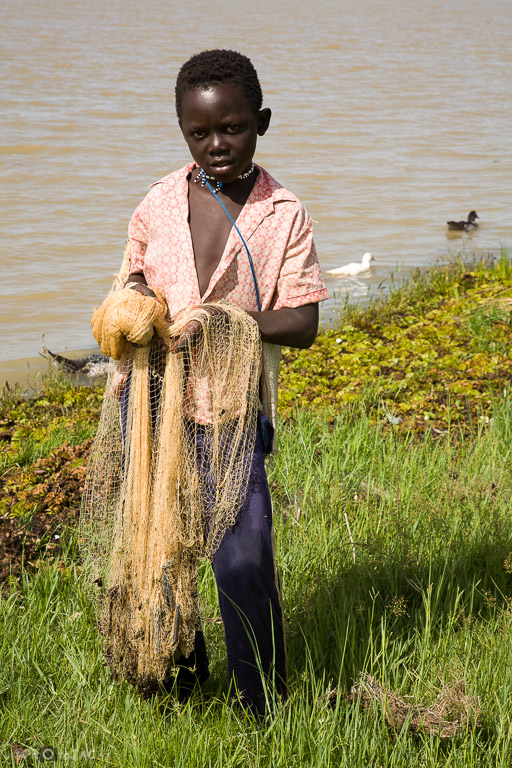 Niño de etnia bozo en una aldea frente a la ciudad de Segou, al otro lado del NIger. Con la red dispuesta para ser lanzada al agua desde la orilla. Mali.