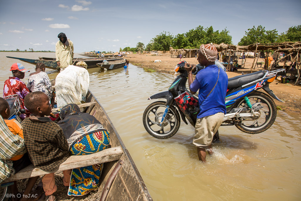 Segou (Mali). Pinaza (embarcación típica de madera) con pasajeros a punto de salir hacia Segou, desde una aldea de etnia bozo situada en la orilla opuesta. Además de pasajeros se aprecia cómo cargan una motocicleta. Mali.