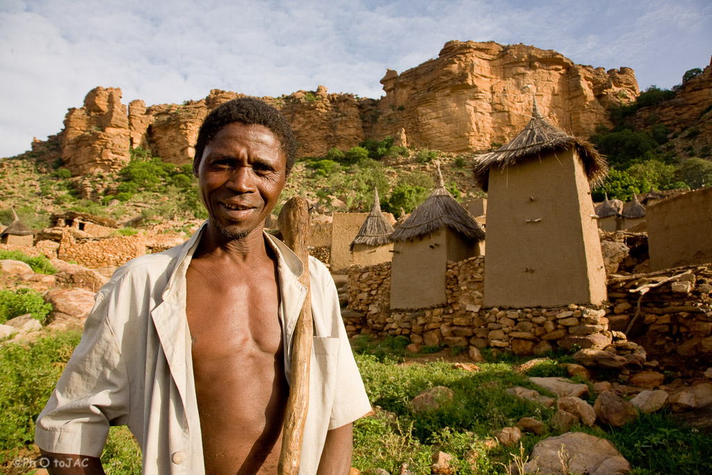 País Dogón. Mali. Campesino de la aldea de Tireli. Tras él, viviendas y graneros erigidos con madera, adobe y piedra. Al fondo la falla de Bandiagara.