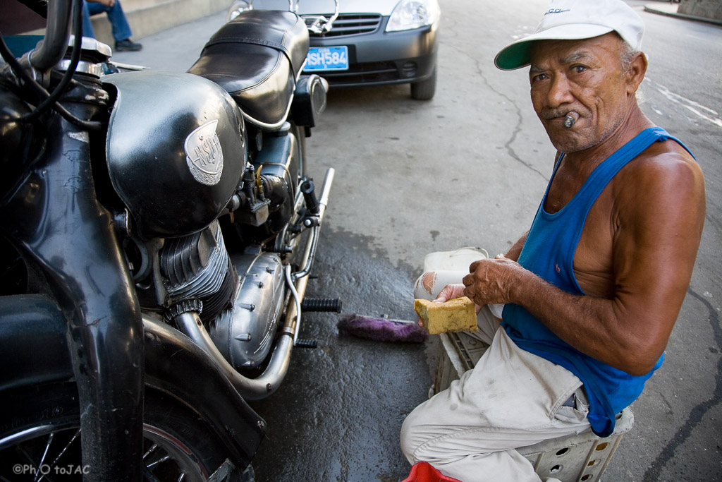 Hombre reparando su motocicleta mientras fuma un "habano". Calles de Centro Habana.