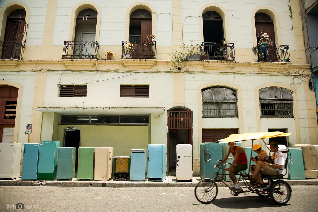 Santiago de Cuba. Sustitución de antiguas neveras rusas. Un bici-taxi pasa por delante de ellas.