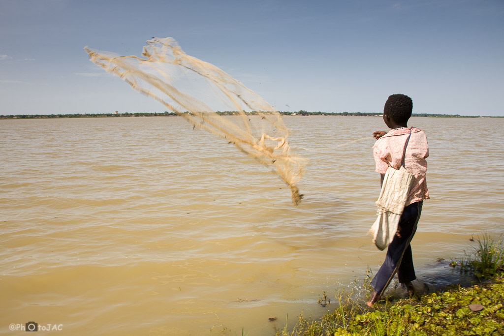 Niño de etnia bozo en una aldea frente a la ciudad de Segou, al otro lado del NIger. Está lanzando una red de pesca al agua desde la orilla. Mali.