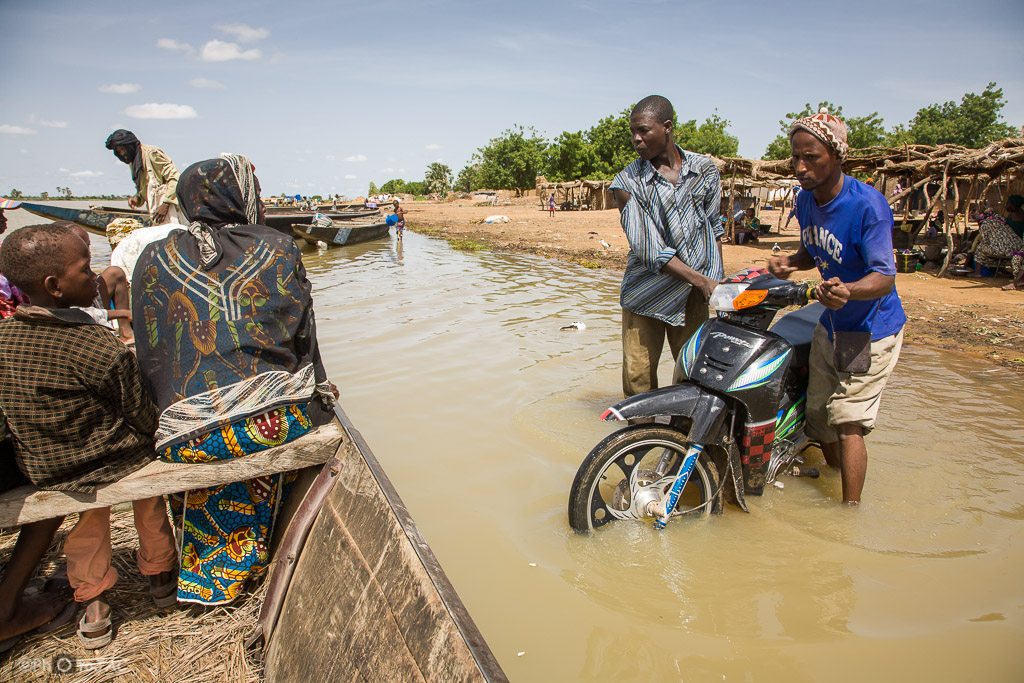 Segou (Mali). Pinaza (embarcación típica de madera) con pasajeros a punto de salir hacia Segou, desde una aldea de etnia bozo situada en la orilla opuesta. Además de pasajeros se aprecia cómo cargan una motocicleta. Mali.