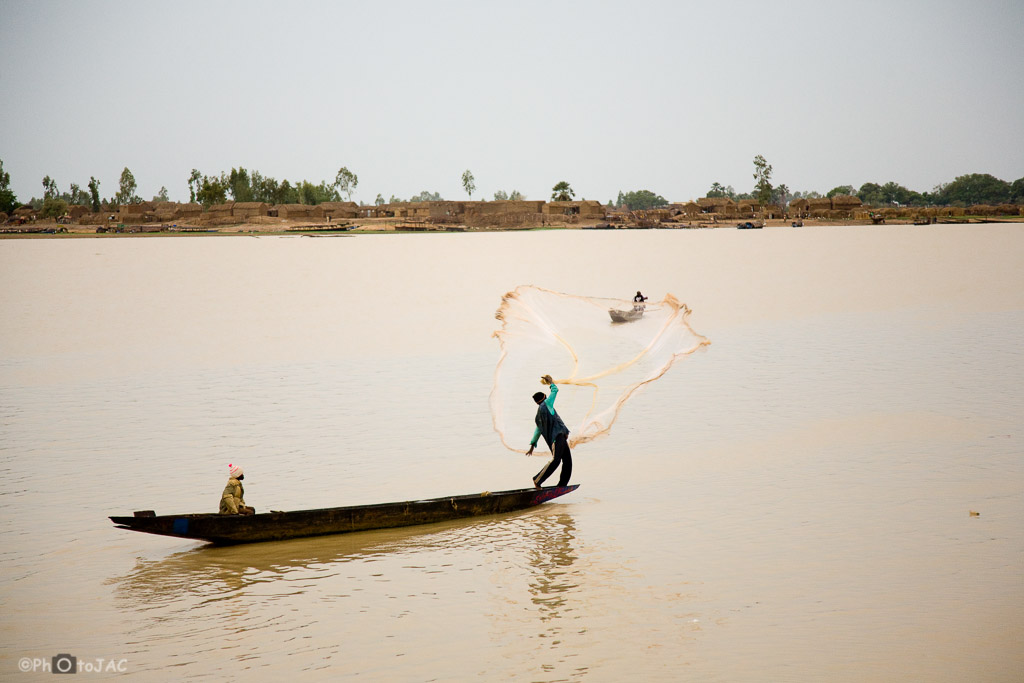Mali: Puerto de Mopti. Embarcaciones locales hechas de madera llamadas "pinazas". Un pescador, de etnia bozo, lanza su red al río Niger. Al fondo un poblado de la etnia bozo (pescadores)