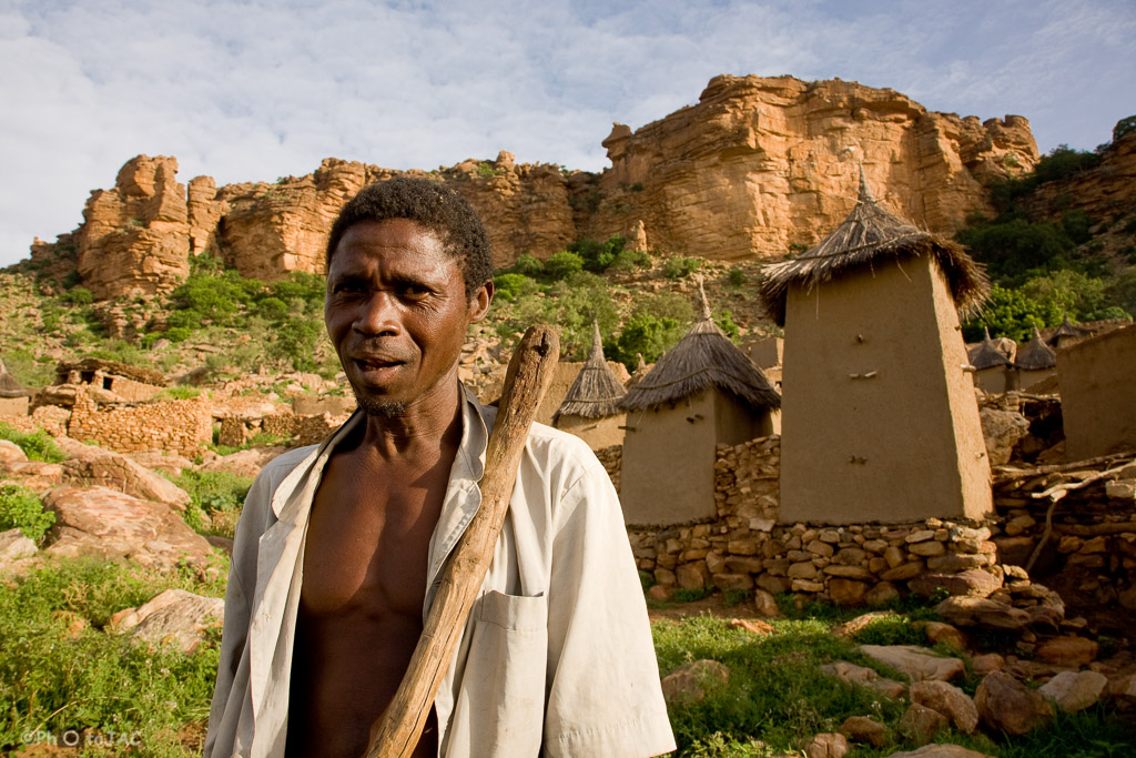 País Dogón. Mali. Campesino de la aldea de Tireli. Tras él, viviendas y graneros erigidos con madera, adobe y piedra. Al fondo la falla de Bandiagara.