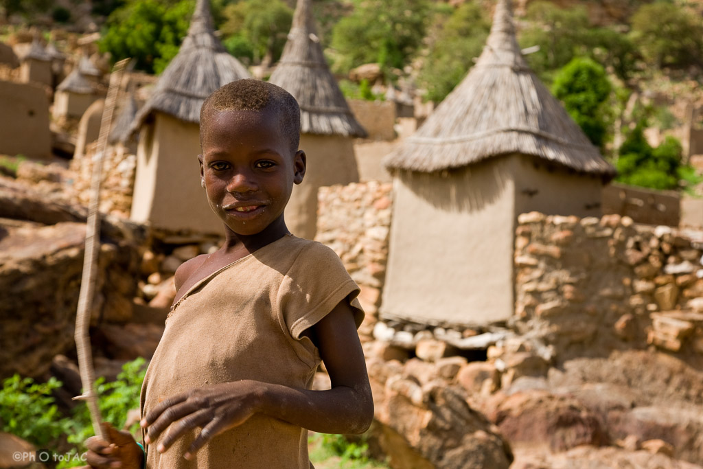 País Dogón. Mali. Aldea de Tireli. Niño de la aldea. Tras él, viviendas y graneros erigidos con madera, adobe y piedra.